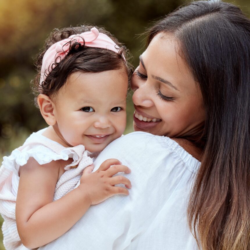 Young Latinx mother holds little girl who smiles at the camera.