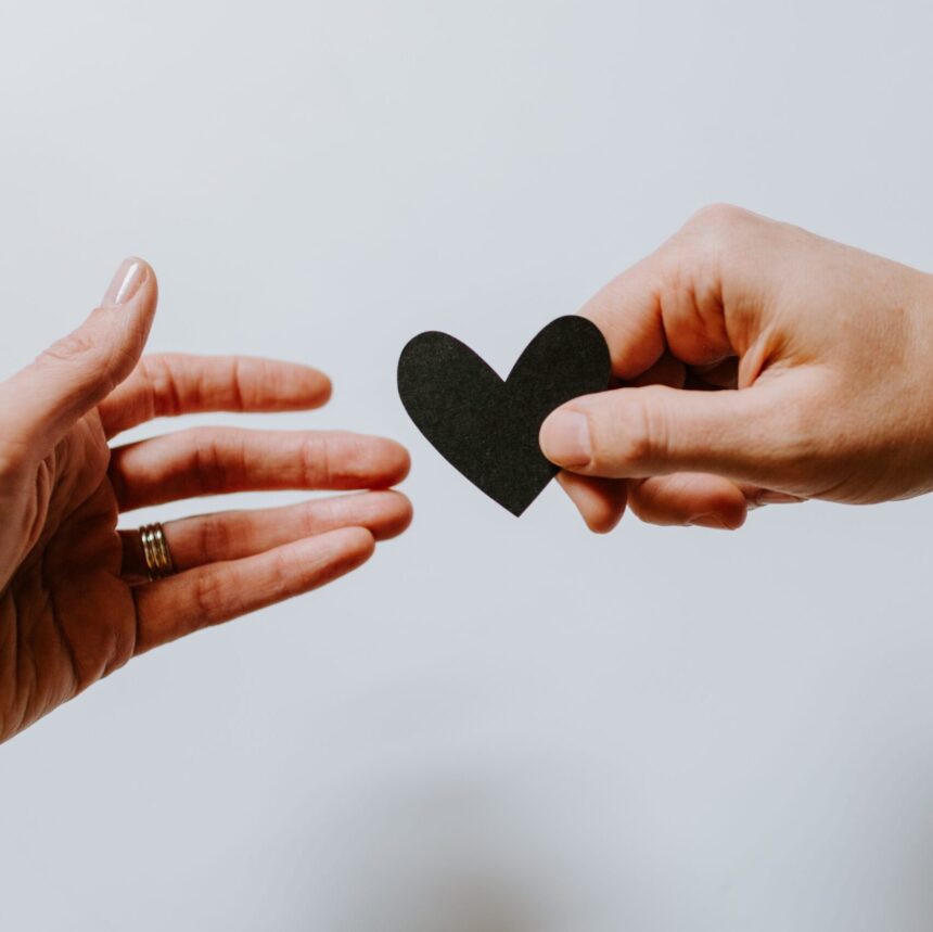 Two people pass a small, black paper or felt heart between their hands.