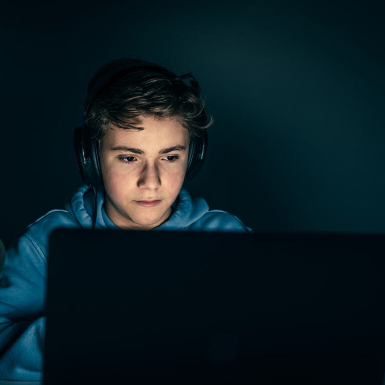 A kid sits in front of a laptop computer, focusing on the glowing screen.